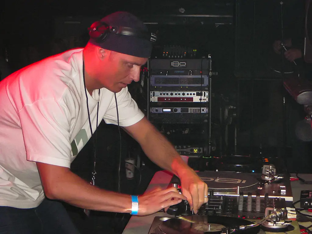 A DJ adjusts the levels on a mixer in the middle of two turntables.